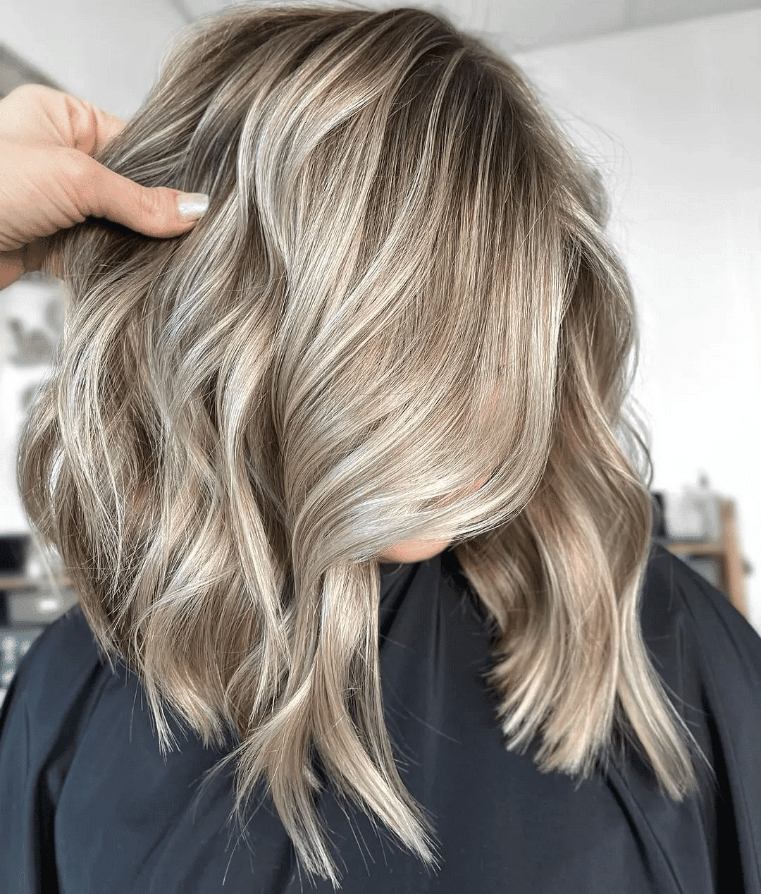 Woman with wavy blonde hair in salon, highlighting fresh highlights and stylish haircut.