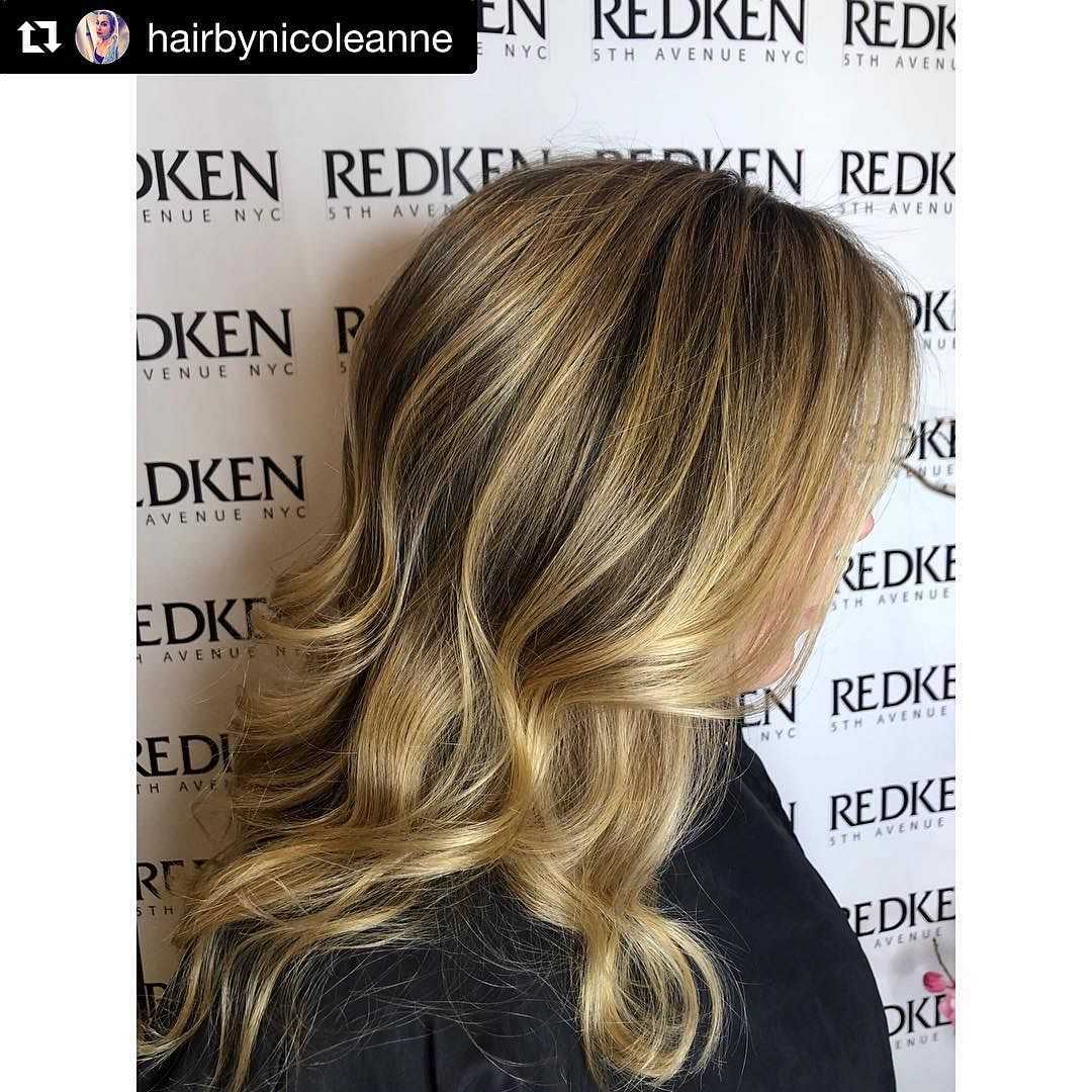 Blonde hair with highlights, styled in loose, soft waves, showcased against a Redken backdrop.