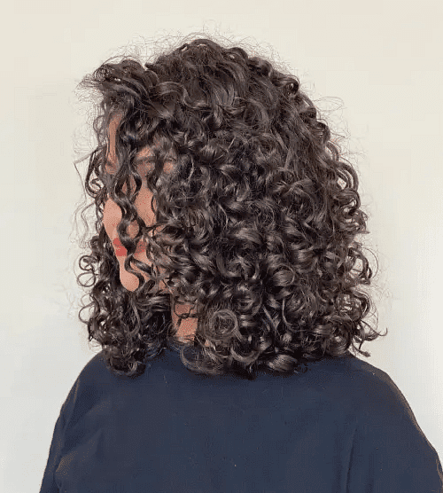 Person with short, curly hair facing sideways, showcasing defined ringlets against a plain background.