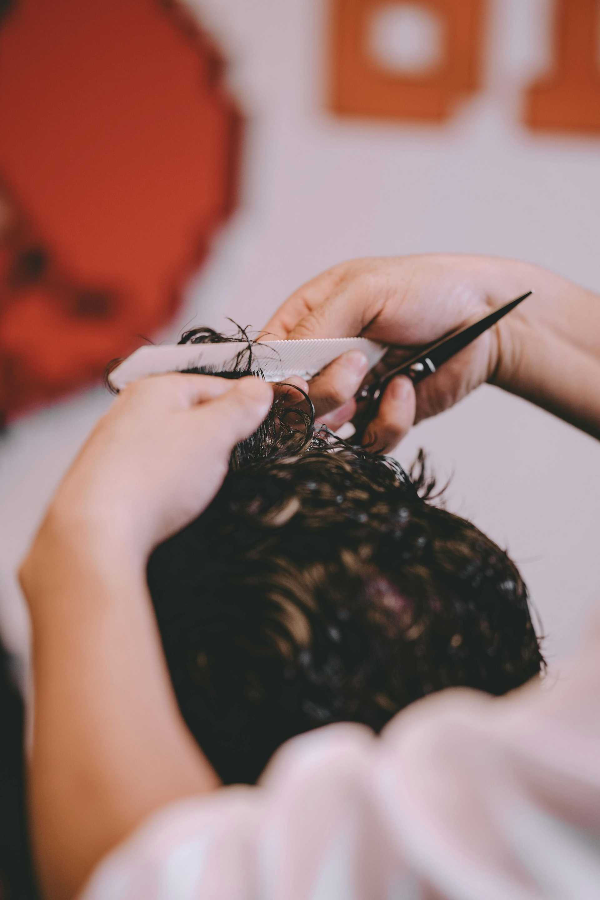 Person getting a haircut with scissors and a comb in a salon setting.